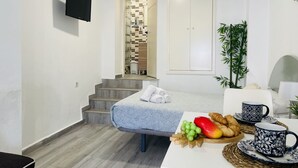 A hotel room with a bed, a small table with breakfast items, a TV mounted on the wall, and a staircase leading to a bathroom.