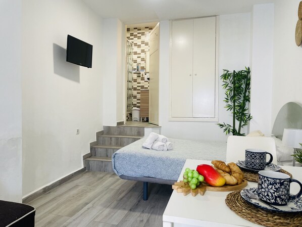 Habitación de hotel con cama, una mesita con alimentos para el desayuno, un televisor montado en la pared y una escalera que lleva a un baño.