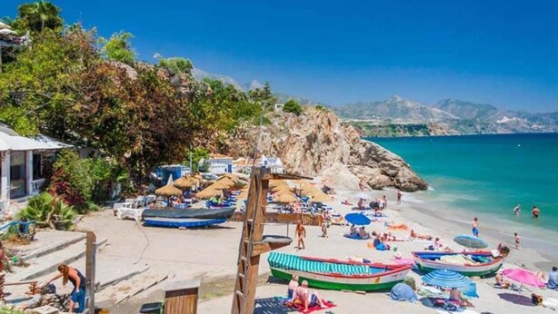 A beach with boats, umbrellas, and people.