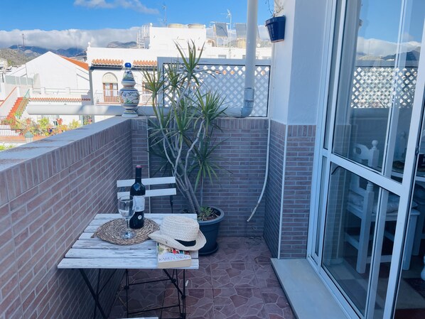 Un balcón con una mesa, una botella de vino, una copa, un libro y una planta en maceta.