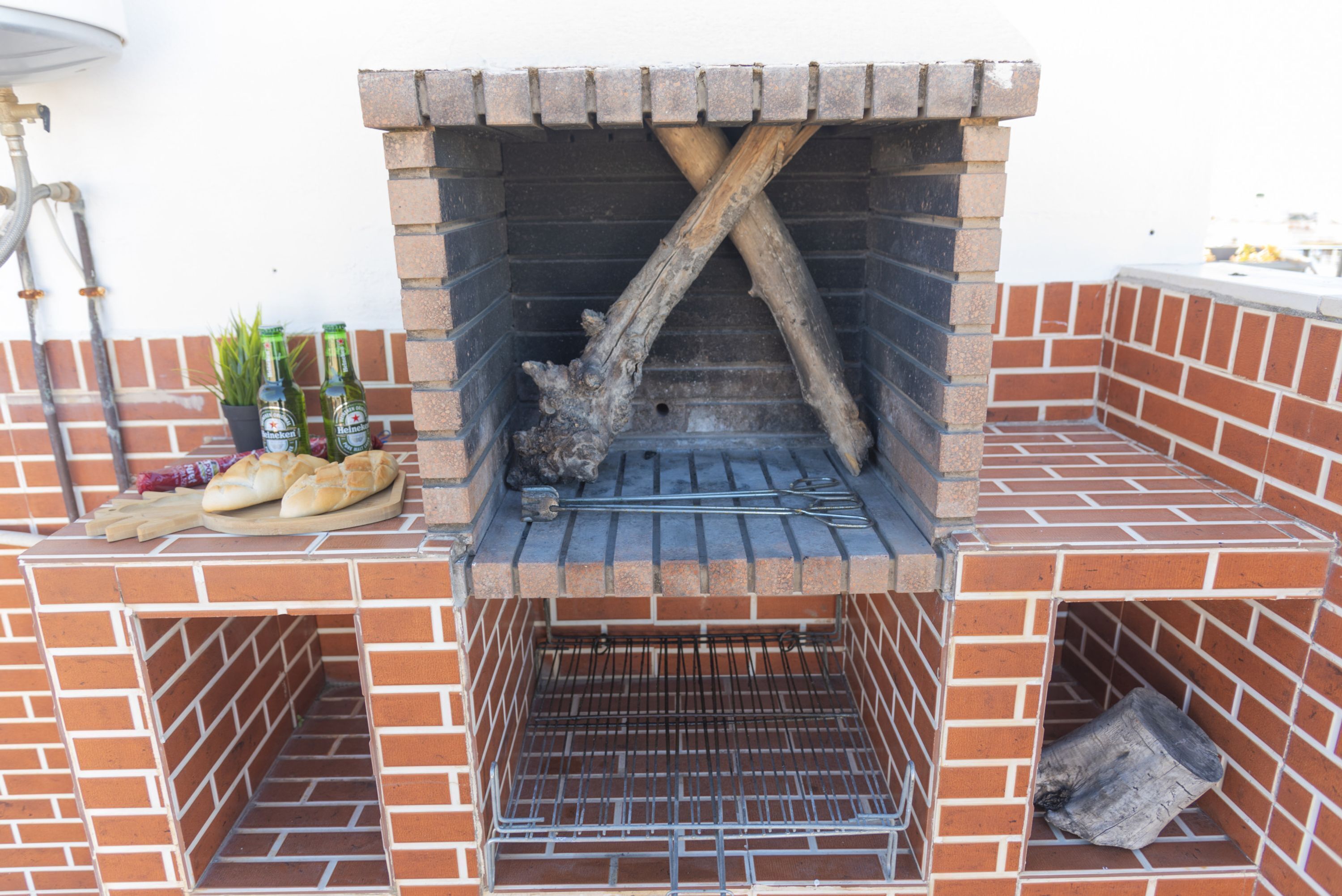 A brick-built outdoor grill with a metal rack and a wooden log support.