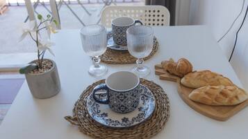 Une table dressée avec deux tasses, deux verres à vin, une assiette de croissants et une orchidée en pot.
