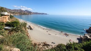 A coastal beach with clear blue waters, rocky cliffs, and a few buildings on the left. - Atico Granada Jimena by At Home Costa del Sol (Nerja)