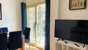 Un salon avec un téléviseur posé sur un meuble, un coin repas avec des chaises et une table, et une porte-fenêtre coulissante donnant sur un balcon.
