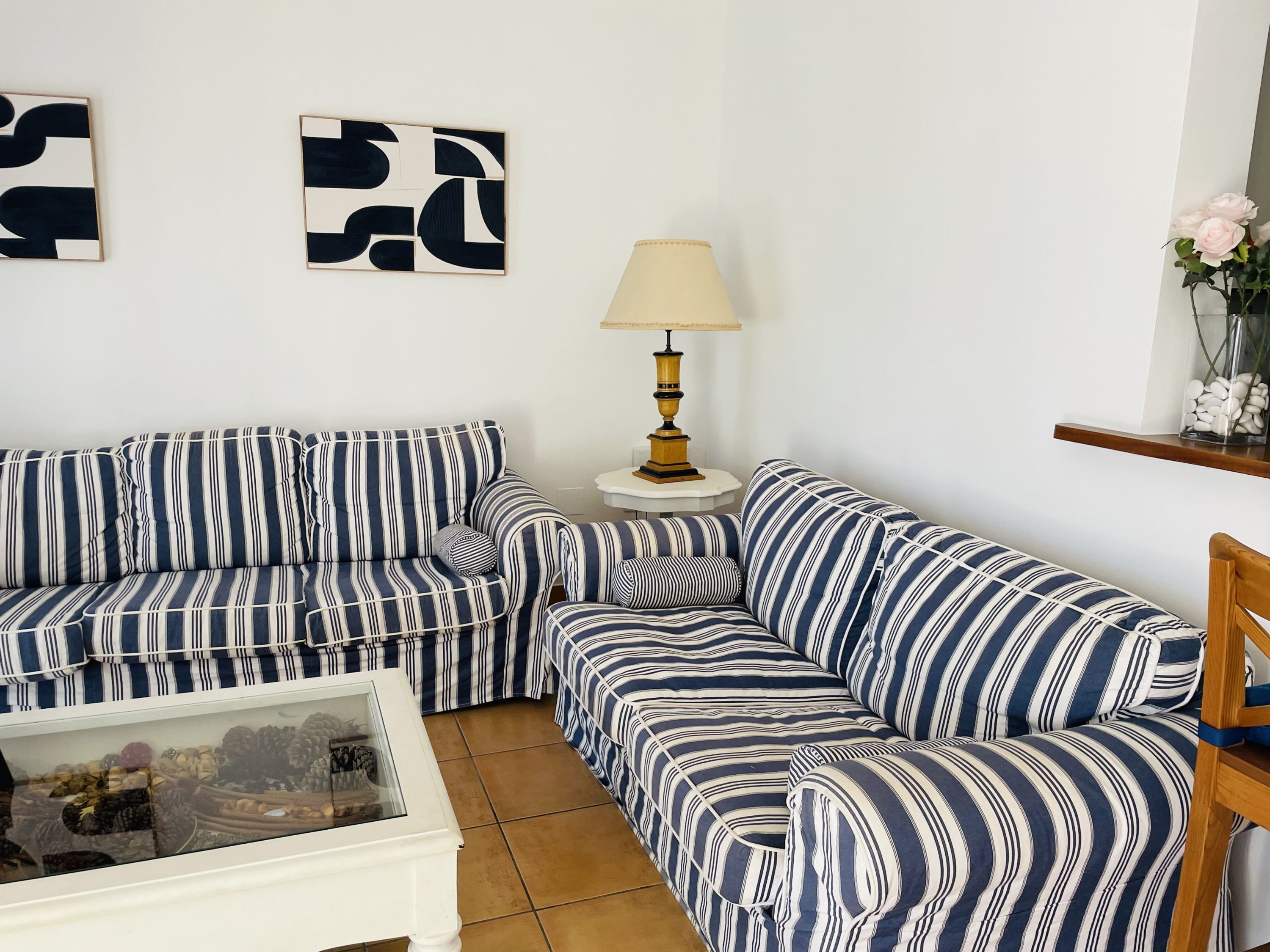 Una sala de estar con sofás a rayas, una mesa de centro de vidrio y una lámpara.