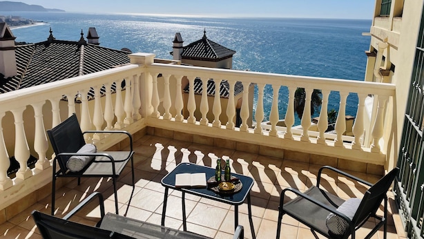Un balcon avec vue sur la mer, comprenant une table, des chaises et des bouteilles.
