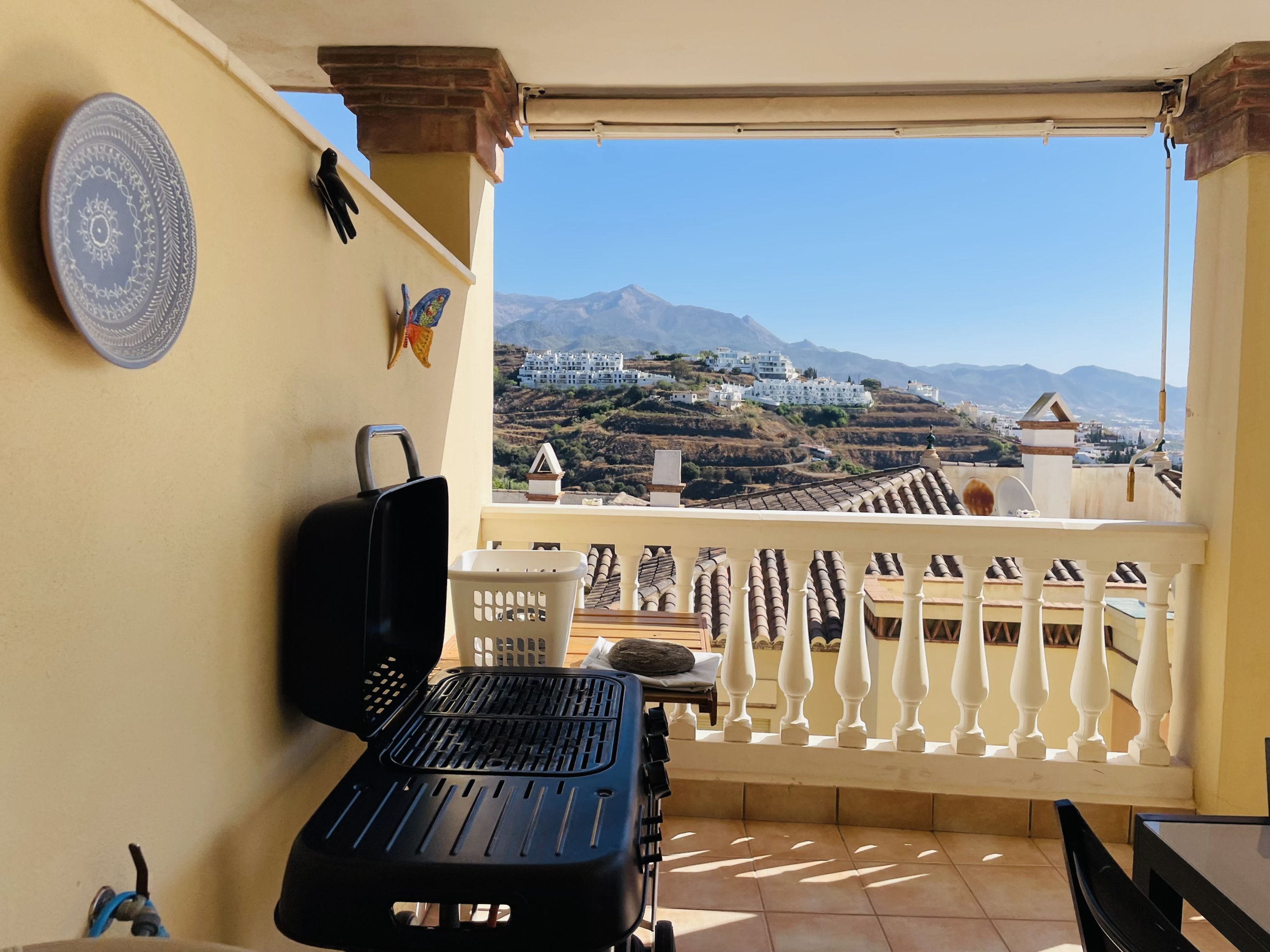 A balcony with a grill, a chair, and a view of a mountainous landscape.