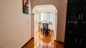 A hallway leading to a dining area with a table and chairs, a painting on the wall, and a door on the right. - Apartamento Faro Torrox by At Home Costa del Sol (Torrox)