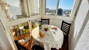 A sunlit dining area with a table set for two, featuring a floral tablecloth, a vase with flowers, and a plate of food including bread and apples. - Apartamento Faro Torrox by At Home Costa del Sol (Torrox)