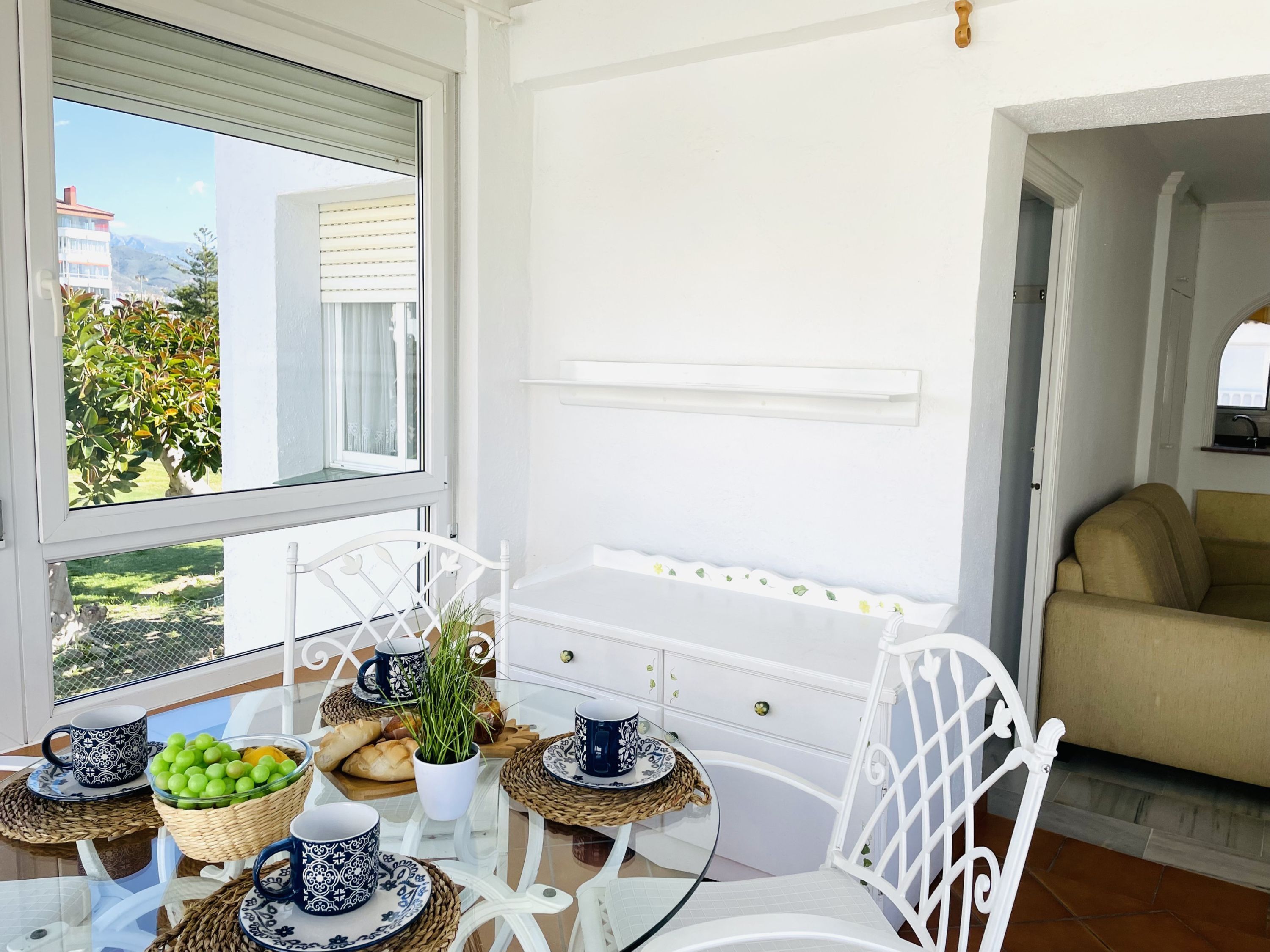 Une pièce lumineuse et ensoleillée, avec une table à manger dressée pour le petit-déjeuner, agrémentée d’un panier de fruits, de pain et d’une plante en pot.