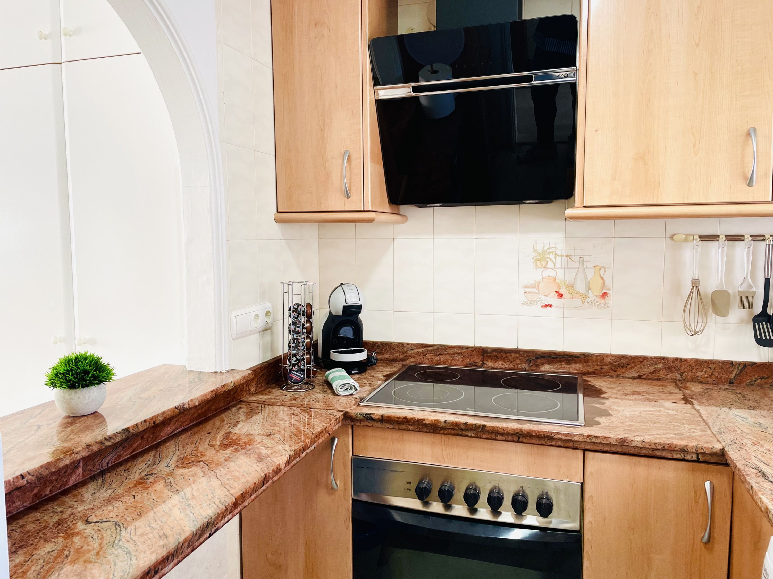Une cuisine avec des meubles de rangement en bois, un micro-ondes noir, une cuisinière en acier inoxydable et une machine à café.