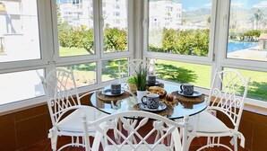 A sunlit room with a glass table surrounded by white chairs, overlooking a residential area with buildings and greenery. - Apartamento Laguna Beach by At Home Costa del Sol (Torrox)