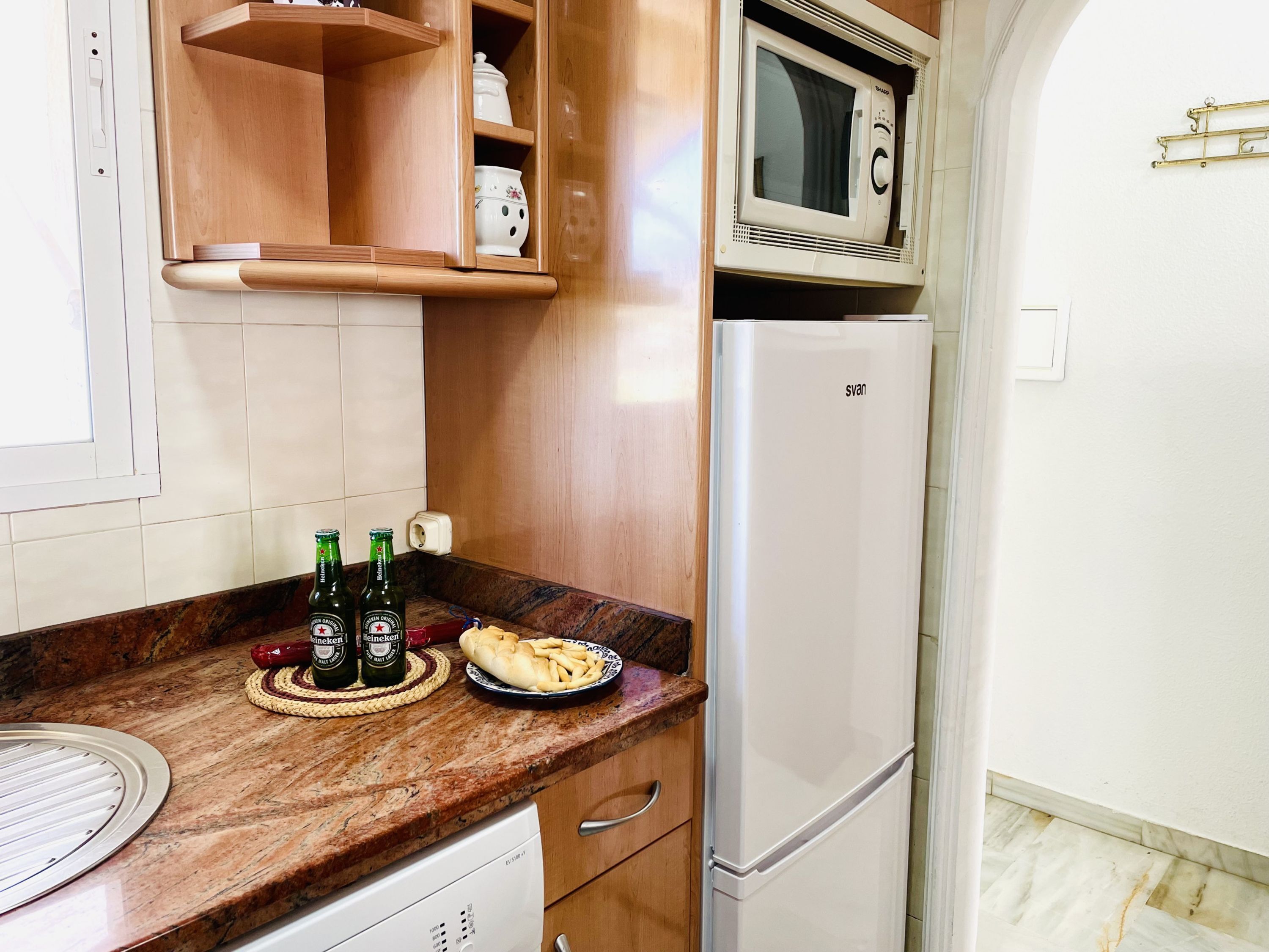 Une cuisine équipée d’un four à micro-ondes, d’un réfrigérateur, de meubles en bois et d’un plan de travail en marbre.