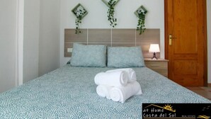 A bedroom with a bed, two pillows, a nightstand, a lamp, and a wooden door. - Apartamento Huelva Jimena by At Home Costa del Sol (Nerja)