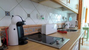 A kitchen with a coffee maker, toaster, and a microwave. There is a sink with a dish rack holding tomatoes. The backsplash is tiled with a diamond pattern. - Apartamento Huelva Jimena by At Home Costa del Sol (Nerja)