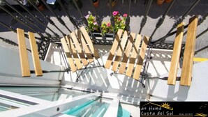 A modern outdoor seating area with wooden slats and metal railings, overlooking a pool and potted plants. - Apartamento Huelva Jimena by At Home Costa del Sol (Nerja)