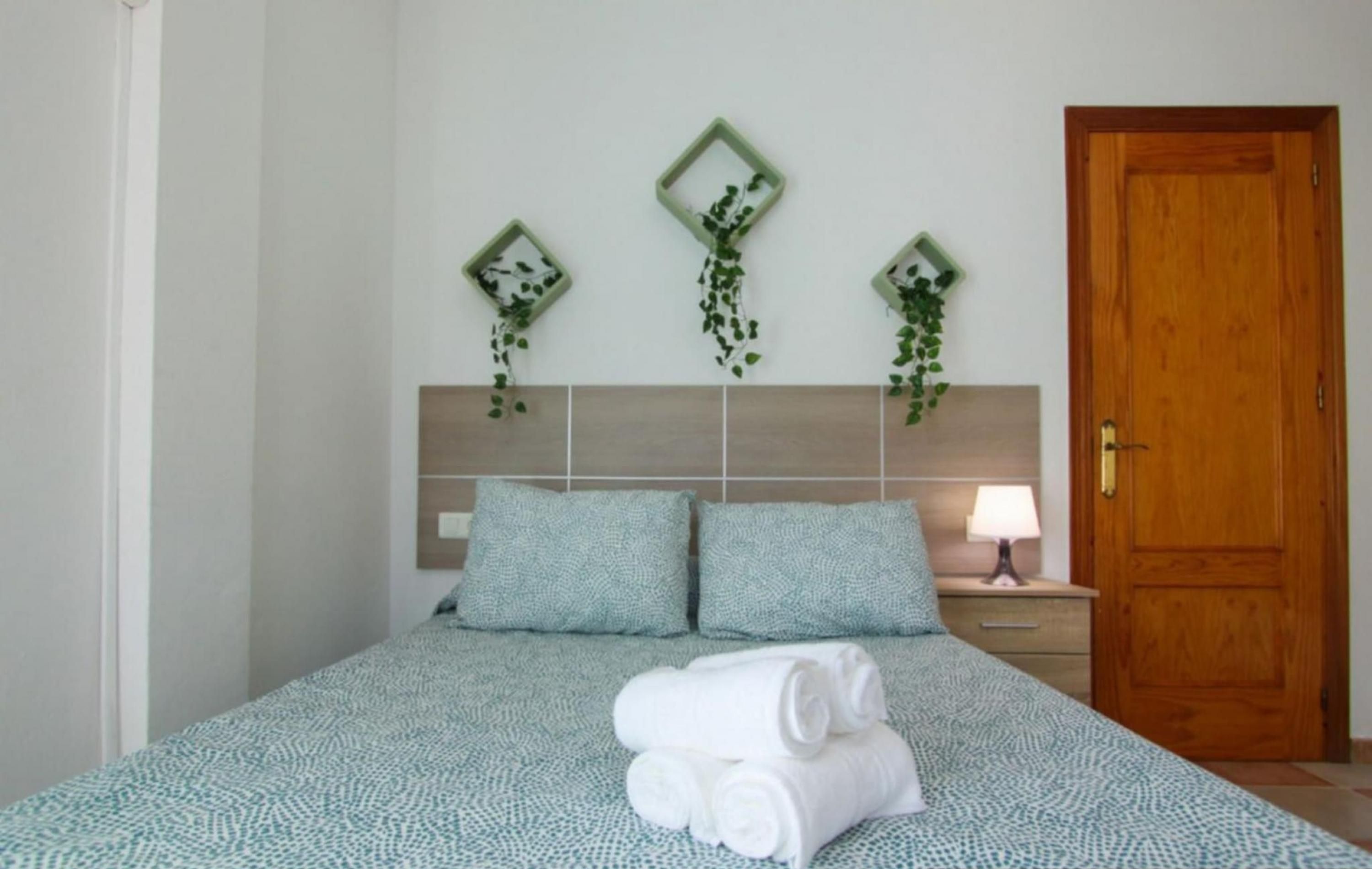 A bedroom with a bed, two pillows, a nightstand, a lamp, and a wooden door.