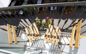 Un área de estar exterior moderna con listones de madera y barandillas metálicas, con vistas a una piscina y plantas en macetas.