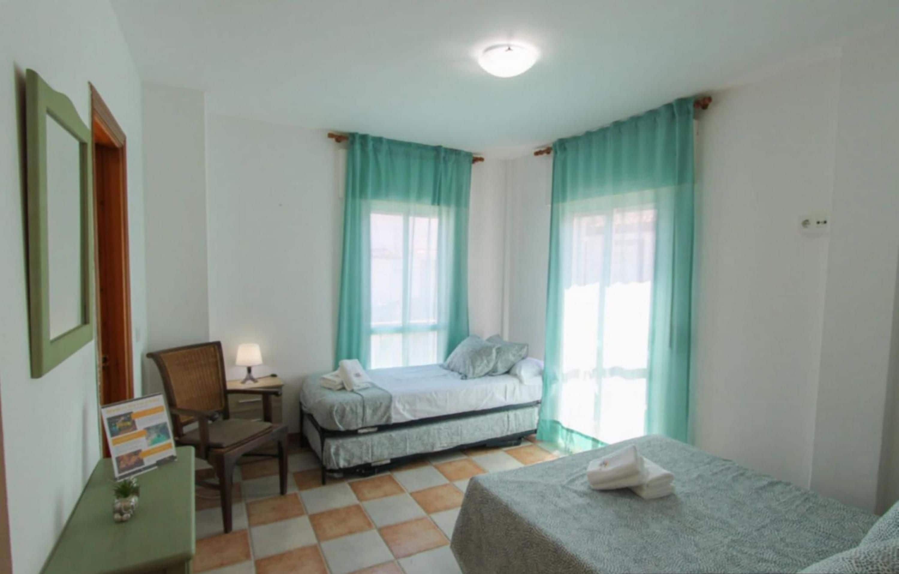 Une chambre avec deux lits, un bureau, une chaise et une fenêtre avec des rideaux.