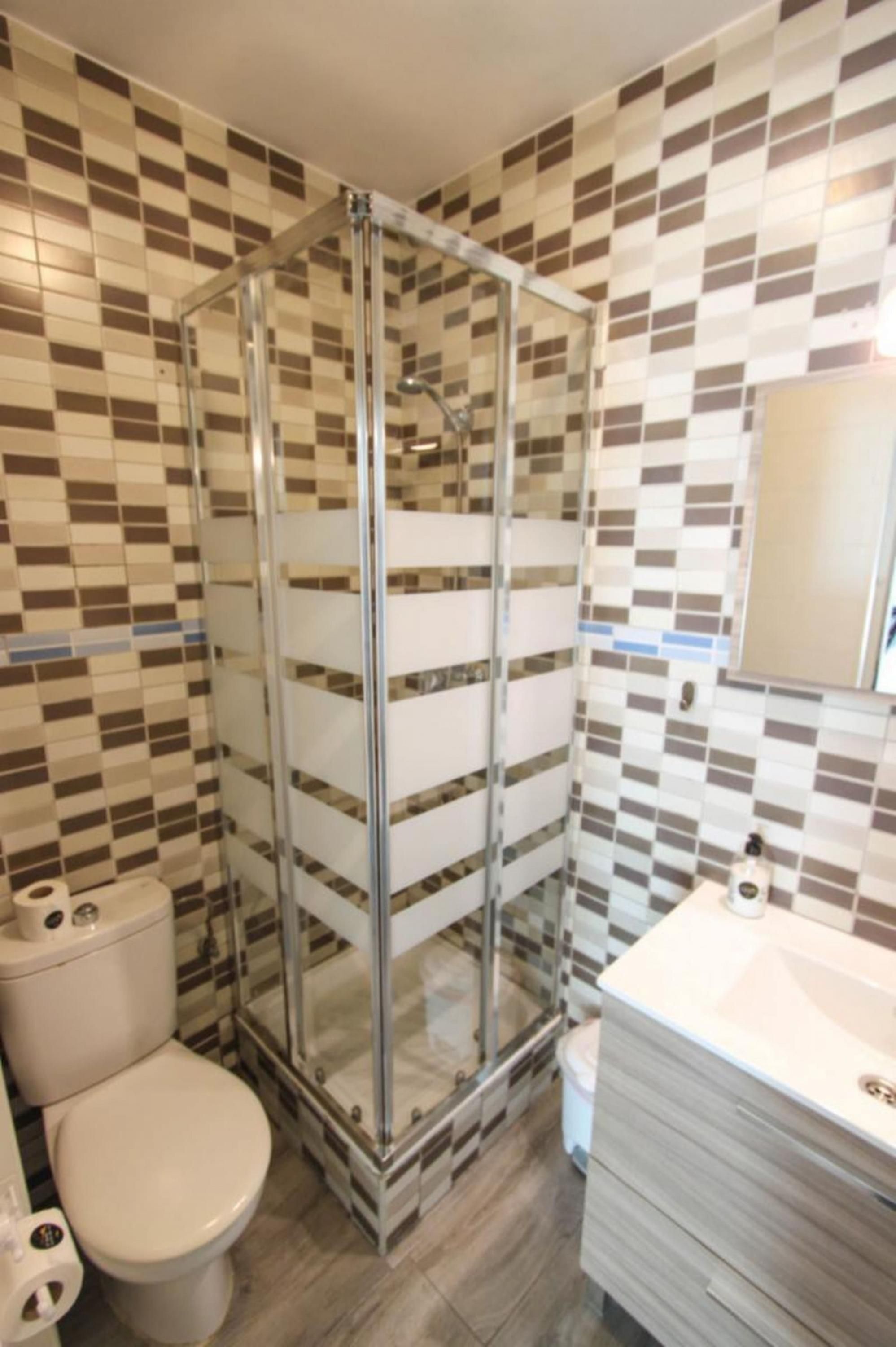 A bathroom with a glass-enclosed shower, a toilet, and a sink with a mirror.
