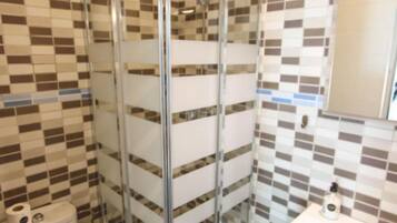 A bathroom with a glass-enclosed shower, a toilet, and a sink with a mirror.