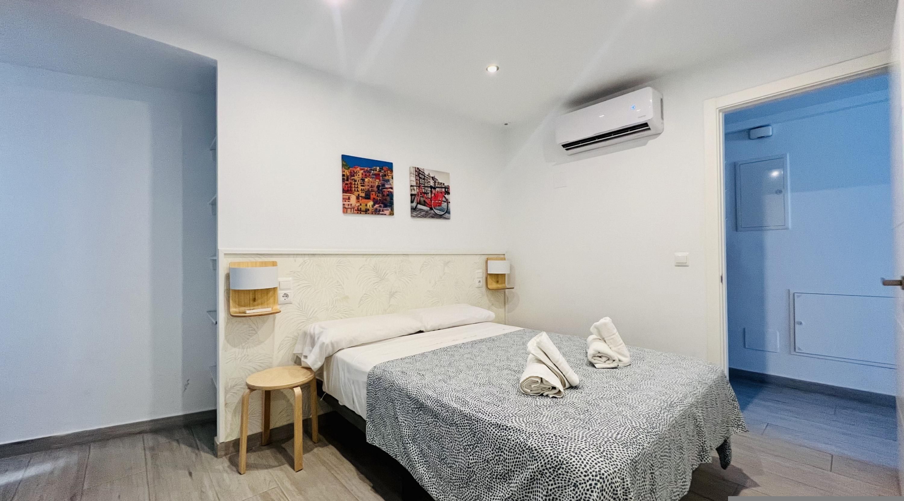 Ein Hotelzimmer mit Bett, Nachttisch, Wandklimaanlage und zwei Wandbildern.
