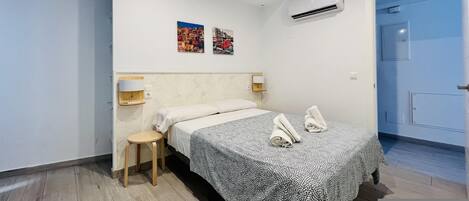 Ein Hotelzimmer mit Bett, Nachttisch, Wandklimaanlage und zwei Wandbildern.