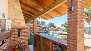 A covered outdoor bar area with a pool view, a stone wall, and a brick column. - Villa La Coscoja by At Home Costa del Sol (Torrox)