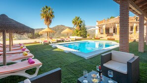 A pool area with lounge chairs, a table with drinks, and a building in the background. - Villa La Coscoja by At Home Costa del Sol (Torrox)