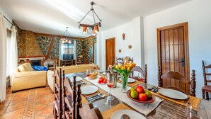 A dining area with a long table set for a meal, surrounded by wooden chairs. - Villa La Coscoja by At Home Costa del Sol (Torrox)