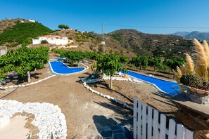 A pool area with a heart-shaped design, surrounded by a white picket fence, and set against a backdrop of hills and a clear sky.