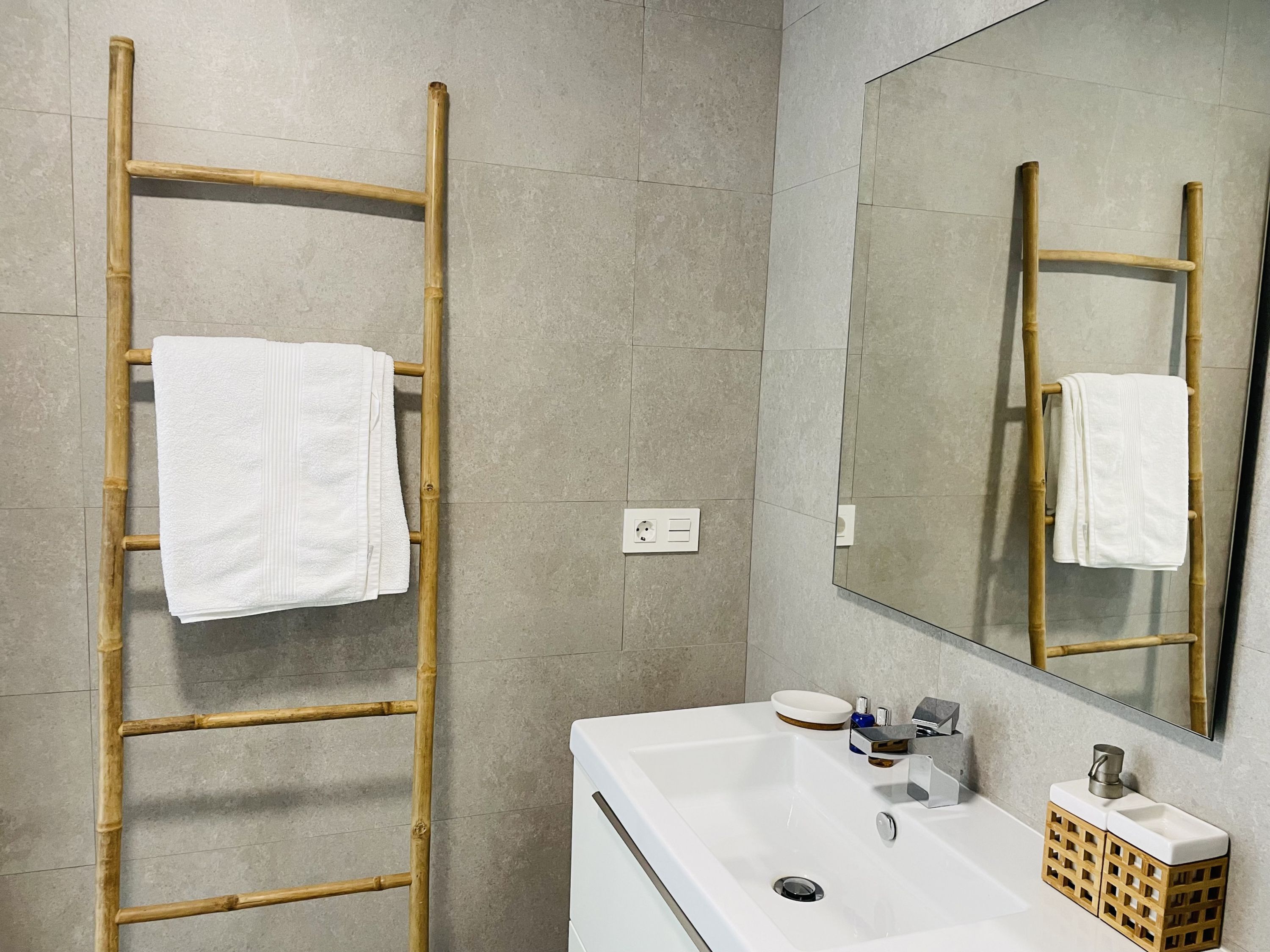 A bathroom with a white sink, a mirror, and a bamboo towel rack.