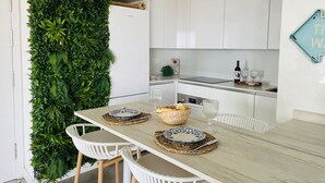 Una cocina moderna con armarios blancos, una mesa de comedor de madera dispuesta con platos, vasos y una cesta de pan.