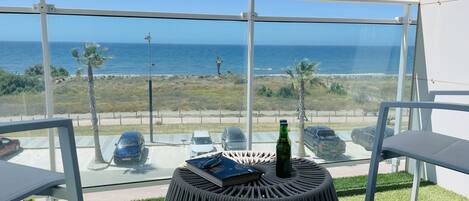 A balcony with a view of the ocean, a round table with a book and a bottle, and a chair.