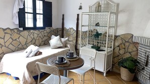 Um quarto aconchegante com uma cama, uma pequena mesa com cadeiras, um armário decorativo e uma parede com padrão de pedra.