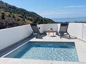 Ein Pool auf dem Dach mit zwei Liegestühlen und einem kleinen Tisch, mit Blick auf eine hügelige Landschaft.