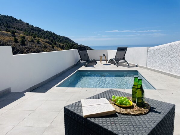 Ein Pool auf dem Dach mit Liegestühlen, ein Tisch mit Buch und Trauben sowie eine Flasche.