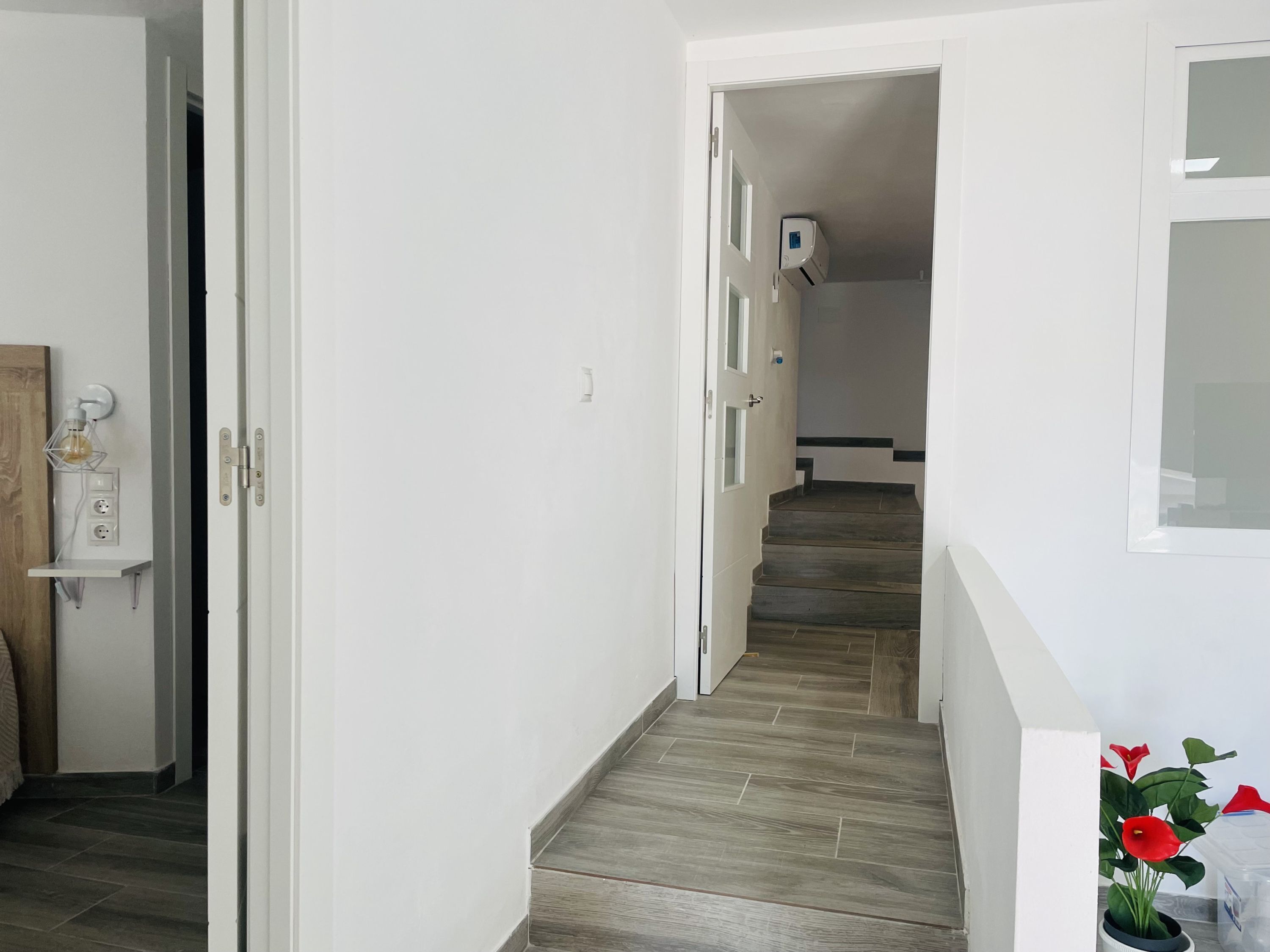 A hallway with a wooden floor, white walls, and a door leading to another room.