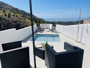 Ein Pool auf dem Dach mit zwei Liegestühlen und einem Tisch, mit Blick auf eine gebirgige Landschaft.