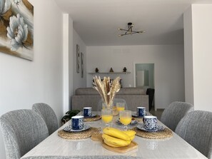 A dining area with a table set for four, featuring blue and white patterned tableware, a vase with pampas grass, and a wooden cutting board with bananas.