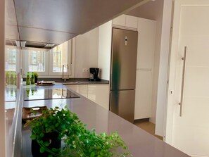 A modern kitchen with a stainless steel refrigerator, a coffee maker, and a large window providing natural light.