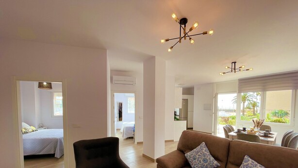 A modern living room with a brown sofa and black armchair, a dining area with a table and chairs, and a kitchen in the background. - Apartamento Torrox Costa a Metros de la Playa (Torrox)