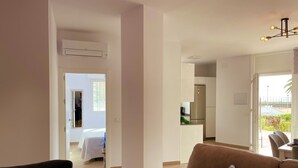 A modern living room with a brown sofa and a patterned pillow, a dining area with a table and chairs, and a kitchen with a refrigerator and cabinets. - Apartamento Torrox Costa a Metros de la Playa (Torrox)