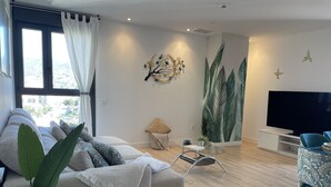 A modern living room with a sofa, a glass coffee table, a TV, and a large window with curtains.