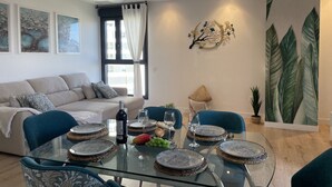 A modern living room with a glass dining table set for four, a sofa, and a large wall mural.
