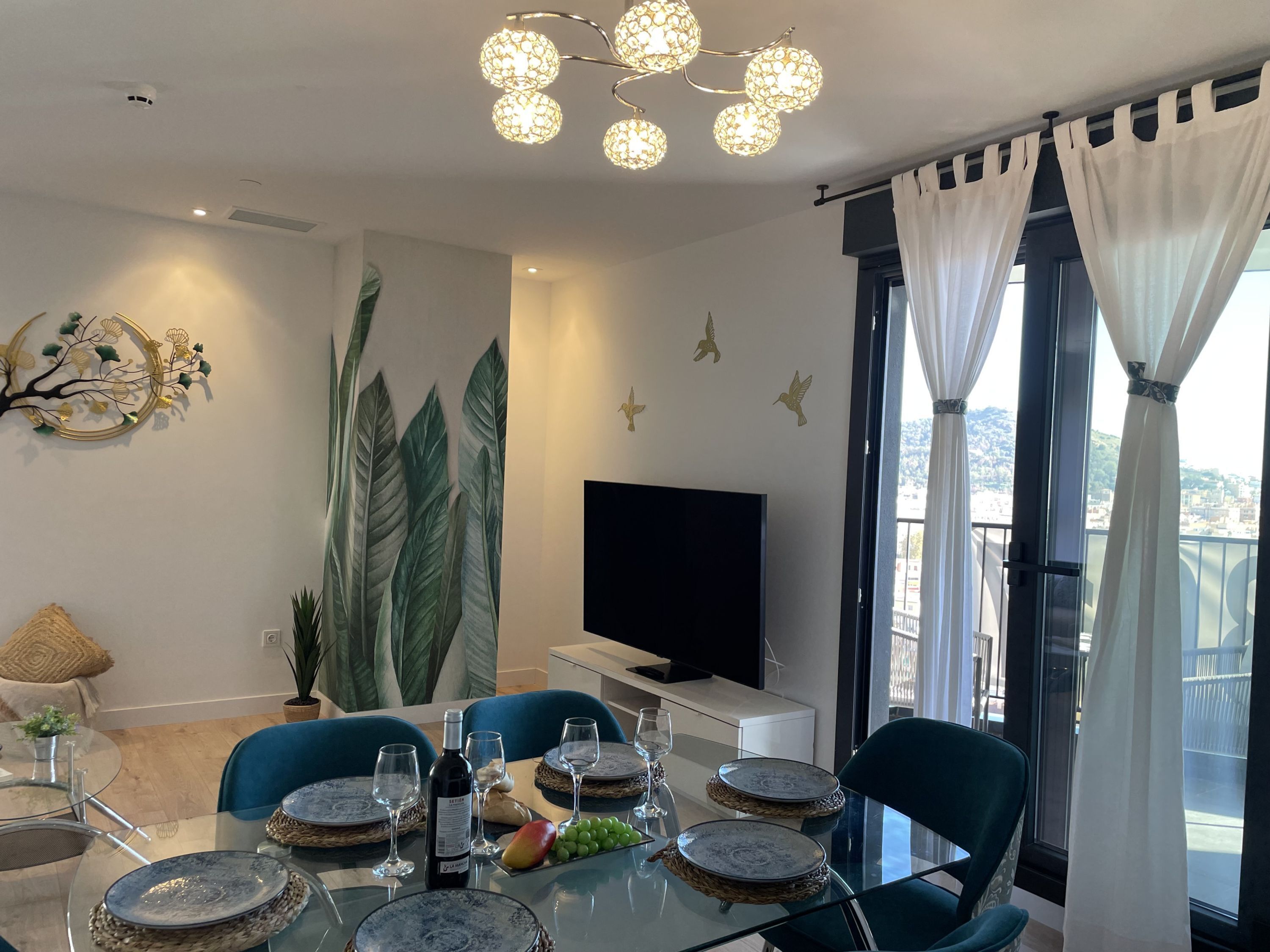 A modern dining area with a glass table, blue chairs, and a decorative wall with leaf patterns.