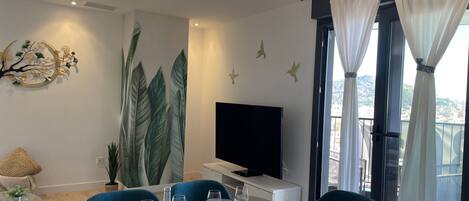 A modern dining area with a glass table, blue chairs, and a decorative wall with leaf patterns.