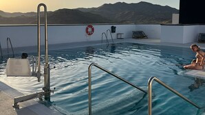 A rooftop pool with a clear view of mountains in the background, a lifebuoy, and a water filtration system.