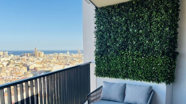 A balcony with a city view, a glass table, and wicker chairs.