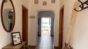 A hallway with a wooden bench, a framed informational sign, decorative wall art, and a vase with reeds. - Casa Paquita con Piscina Privada en Maro By At Hom (Nerja)